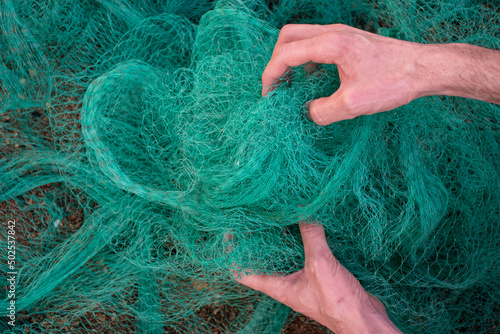 View of a man hands picking up a green fishing net. Waste in nature. Environmental Protection. photo