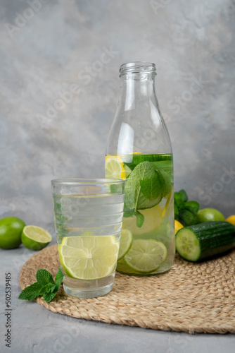 Detox Sassy water with lemon, cucumber, mint. A bottle of clean, cool and fresh drink stands on a gray concrete background with ingredients on board. Strengthening immunity, diet.