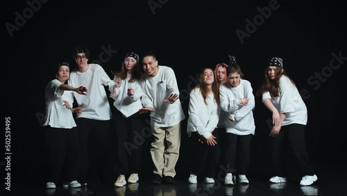 A group of young dancers in white T-shirts on a black background perform free dance movements, they finish the dance with a synchronized final pose photo