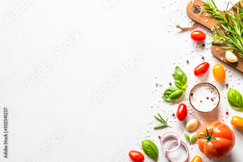 Ingredients for cooking on white stone table. Vegetables, herbs and spices with wooden cutting board. Top view with space for text.