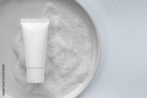 Top down view mockup organic gentle facial skincare product cleanser white tube bottle with soap water bubbles and blank label on white ceramic plate plain grey isolated as a background with space photo