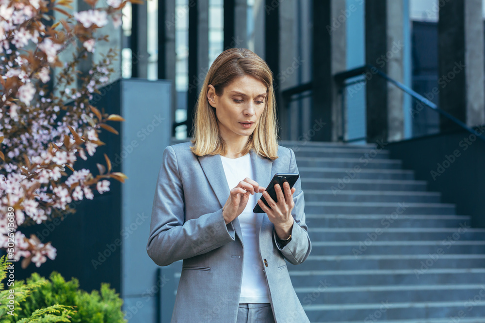 Serious and pensive business woman uses the phone outside the office, looking at the smartphone screen Serious and pensive business woman uses the phone outside the office, looking at the smartphone screen