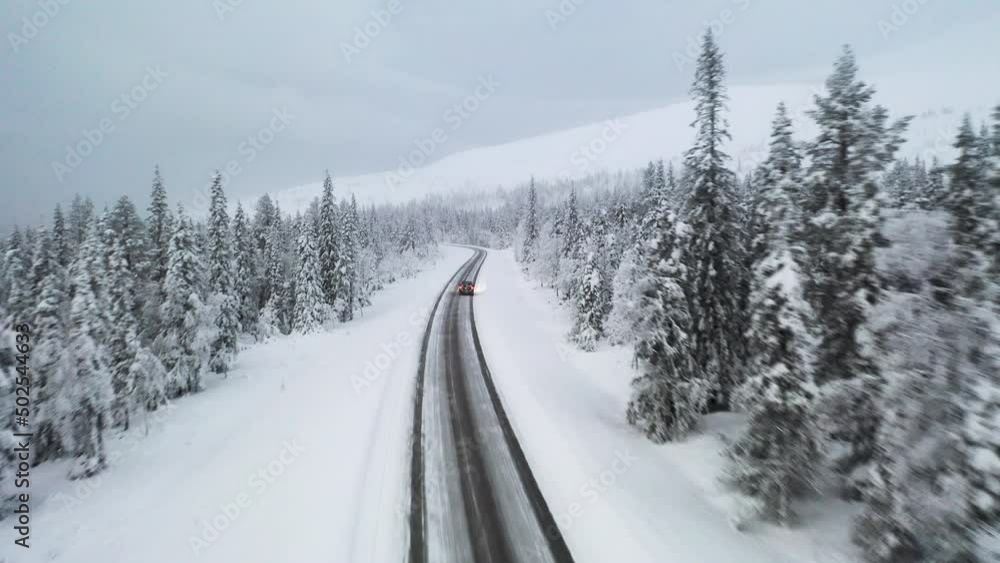 Flying behind a car on a isolated winter road in the middle of snowy forest landscape Flying behind a car on a isolated winter road in the middle of snowy forest landscape