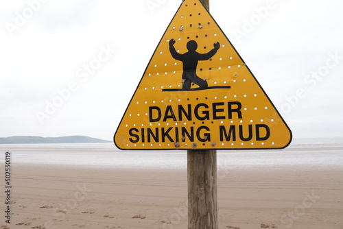 'DANGER SINKING MUD' sign with background of seemingly endless mud where the sea should be