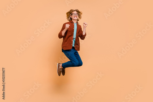 Full length body size view of attractive cheerful lucky guy jumping rejoicing having fun isolated over beige pastel color background