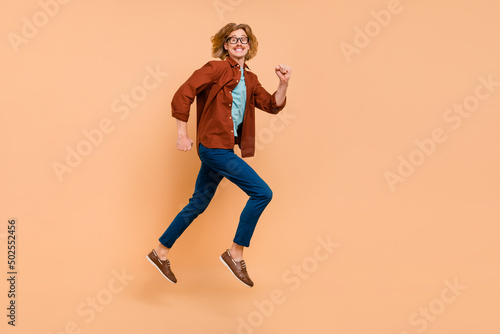 Full length body size view of attractive cheerful motivated guy jumping running isolated over beige pastel color background