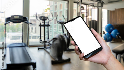 Hand holding smartphone device at gym background. interior of modern fitness center gym