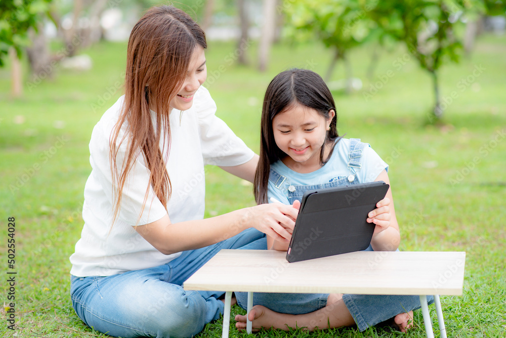 Fototapeta premium A mother is teaching her daughter online on a digital tablet or watching a video clip on a tablet together.