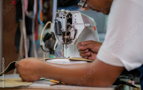 Sewing process of the leather belt. Man's hands behind sewing. Leather workshop.