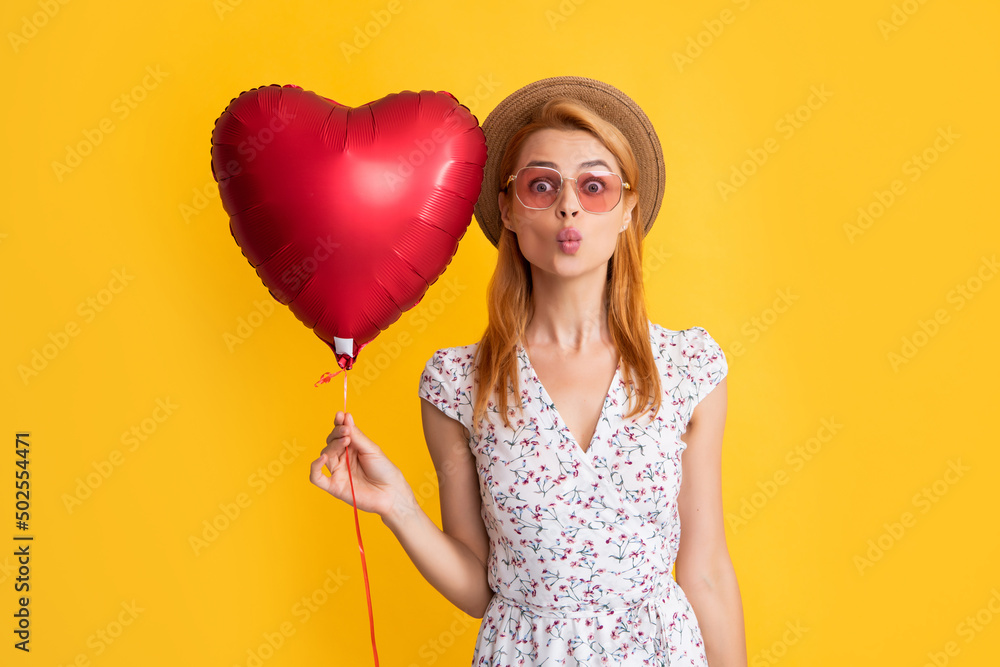 positive young woman in straw hat and sunglasses hold love heart balloon on yellow background positive young woman in straw hat and sunglasses hold love heart balloon on yellow background