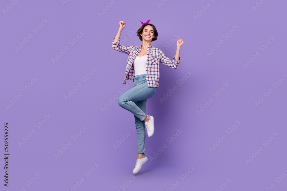 Photo of excited lucky lady dressed checkered shirt rising fists jumping high isolated purple color background Photo of excited lucky lady dressed checkered shirt rising fists jumping high isolated purple color background