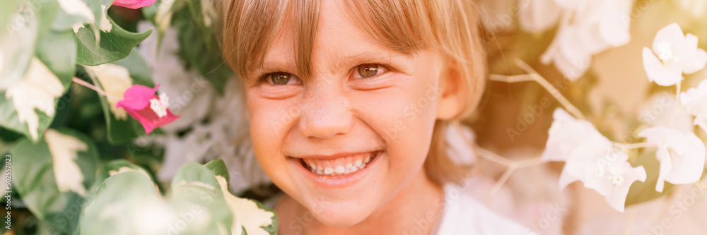 portrait of face candid little happy smiling five year old blonde kid boy with green eyes in pink and white flower plants in nature. children have fun summer holidays. banner. flare portrait of face candid little happy smiling five year old blonde kid boy with green eyes in pink and white flower plants in nature. children have fun summer holidays. banner. flare