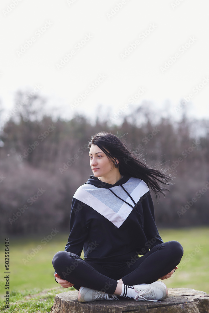 Smiling young woman is sitting in lotus pose on the stump. Meditating outside in spring day. Mental health. Smiling young woman is sitting in lotus pose on the stump. Meditating outside in spring day. Mental health.