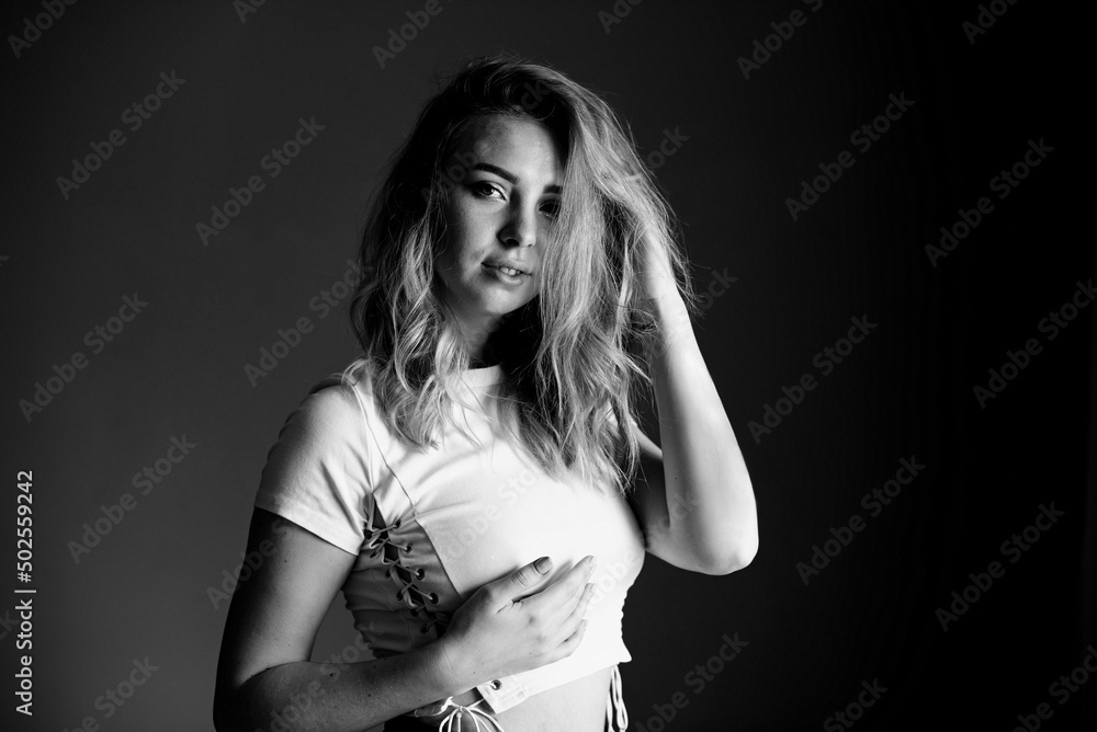 Naklejka premium A girl in a white top with ties straightens her hair and looks at the camera. Black and white photography