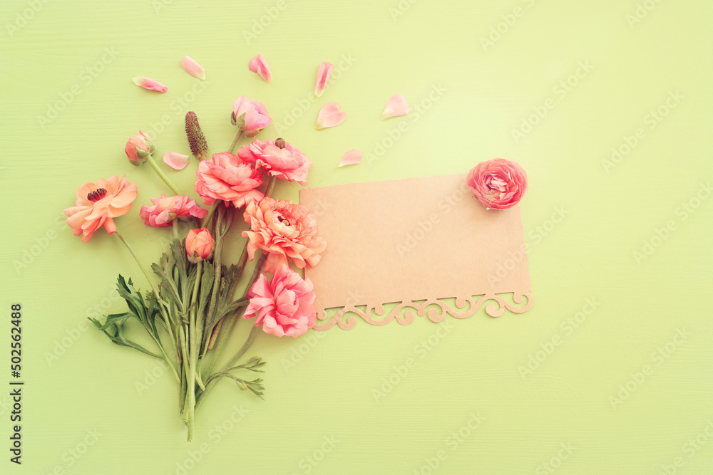 Top view image of pink flowers composition and empty note over green wooden background - obrazy, fototapety, plakaty 