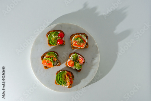 top view open sandwich with fish, toasts with salmon, cherry, microgreens on white marple board white background