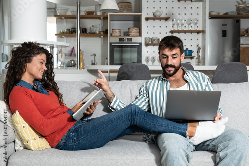 Foto Young couple sitting at home man is bet online on laptop computer on sport and woman is writing and calculating home finances