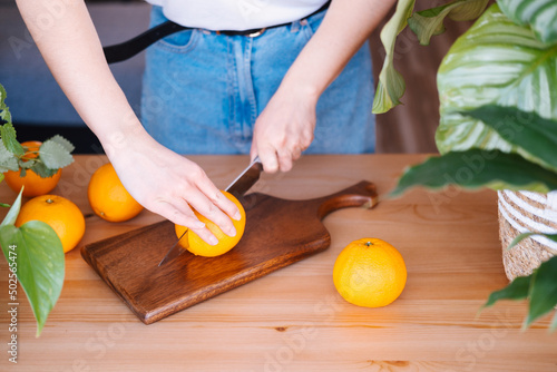 Woman cutting oranges in a kitchen full of plants.
