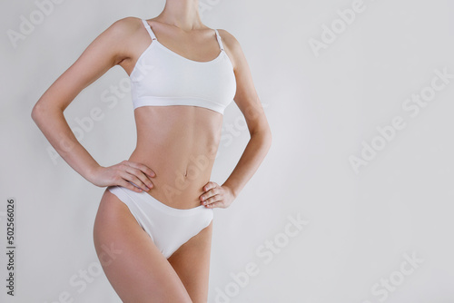 Close up shot of unrecognizable fit woman in lingerie isolated on white background. Torso of slim attractive female with flat belly and thin waist in white underwear. Copy space for text.