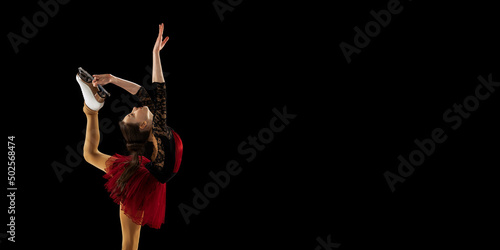 Bilde på lerret Beautiful girl, little female figure skater in beautiful stage attire skating isolated on black background in spotlight