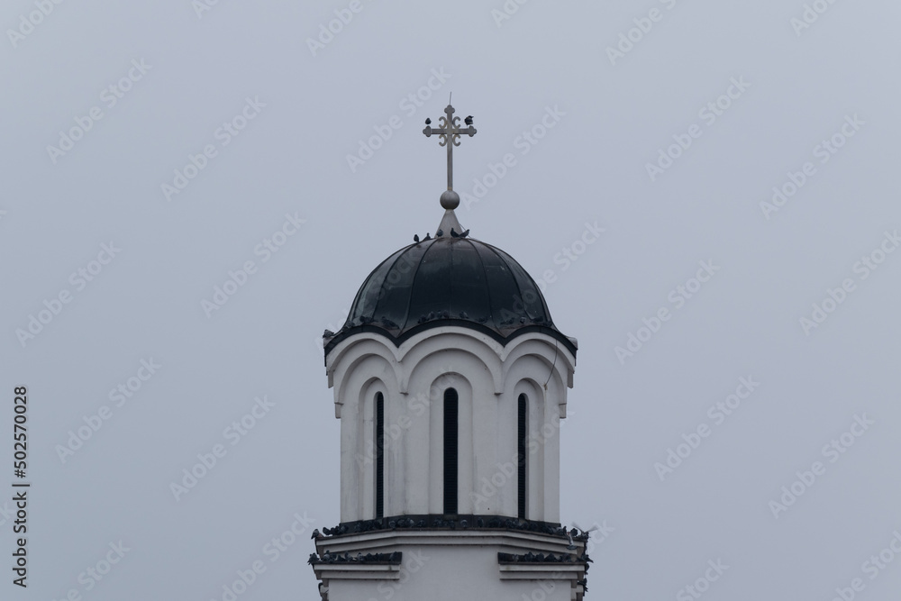 Several pigeons are resting on roof of church bell tower during gloomy cloudy day