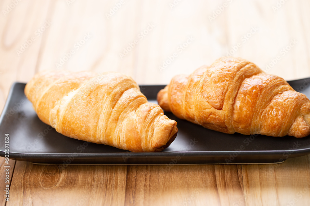 Two croissants are on plate. Croissant is a buttery, flaky, French  pastry. This bread uses the French yeast-leavened laminated dough. Crispy and yummy.