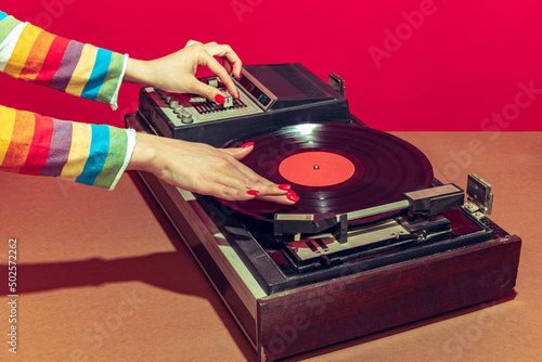 Colorful image of female hands spinning retro vinyl record player like a dj isolated over red background photo