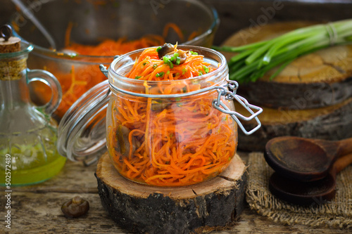 Carrot salad in a glass jar. Carrots in Korean with mushrooms. Wooden background.