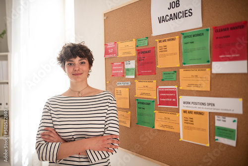 Happy young woman student standing in front of employment noticeboard. photo