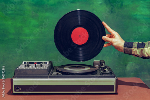 Colorful image of male hand holding retro vinyl record in front of vintage player isolated over dark green background photo