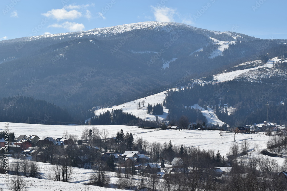 Zimowy krajobraz, stoki narciarskie, śnieg, błękit i chmury.