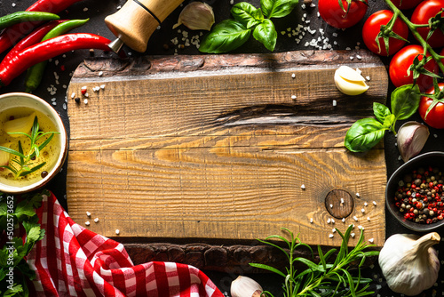 Food background. Oak cutting board, spices and vegetables at dark kitchen table. Top view with space for design.