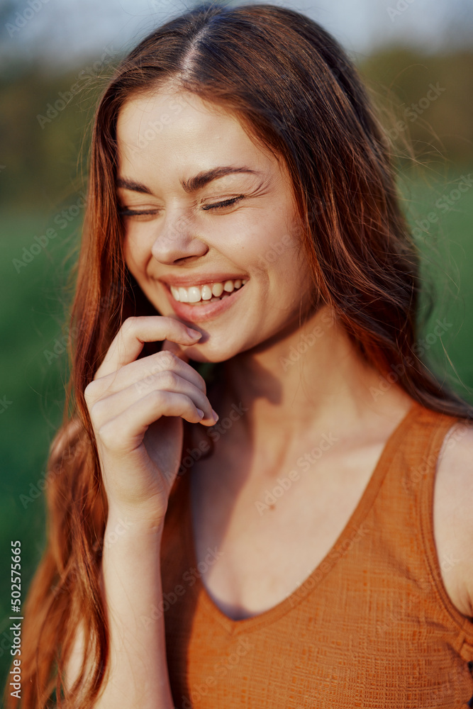 Close-up portrait of a smiling young woman with eyes closed in the sun with red hair in nature Close-up portrait of a smiling young woman with eyes closed in the sun with red hair in nature