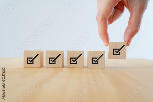 Corporate regulatory and compliance. Quality control management, ISO certification. Product, service quality warranty. Checklist survey and assessment  process. Put wooden cube with check mark icon. photo