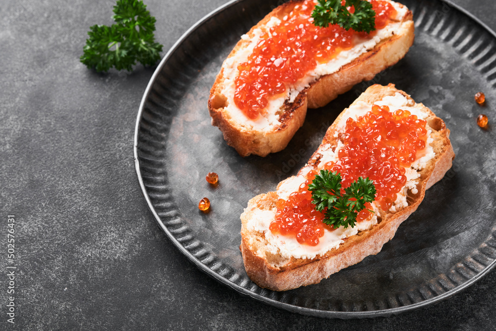 Two dandwiches with red caviar. Salmon red caviar in bowl and sandwiches server on old iron plate on old black table background. Top view. Copy space. Two dandwiches with red caviar. Salmon red caviar in bowl and sandwiches server on old iron plate on old black table background. Top view. Copy space.