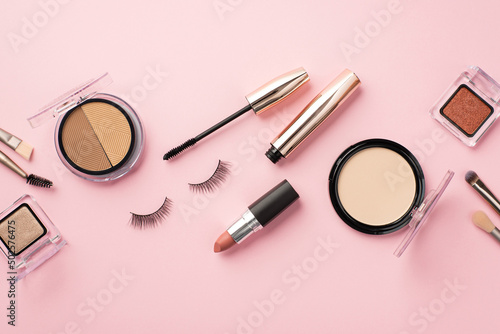 Make up concept. Top view photo of compact powder contouring palette eyeshadow containers makeup brushes lipstick false eyelashes and mascara on pastel pink background