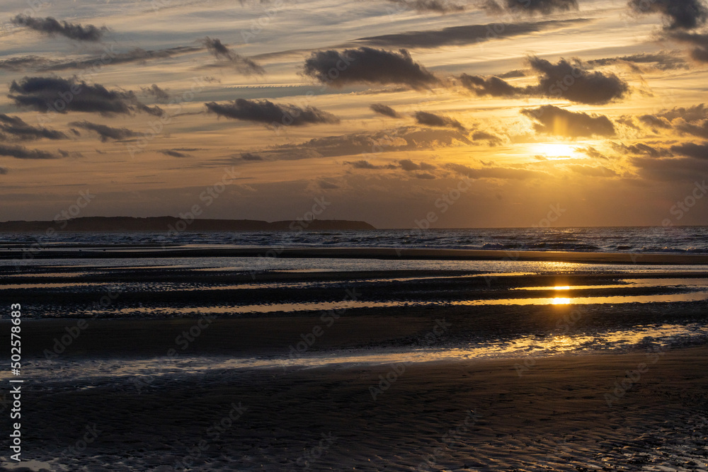 A beautiful, dramatic golden- sunset with some small dark clouds over a beautiful French beach with some small waves rolling in at the shore. High quality photo