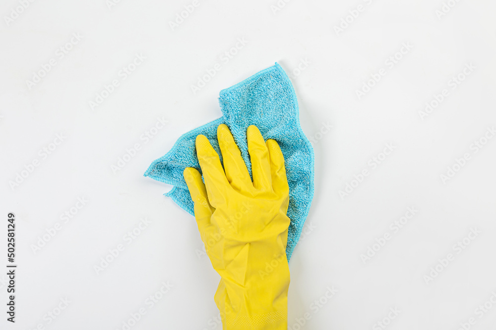 The hand of a housewife in a yellow protective rubber glove holds a rag with microfiber fiber for cleaning agent on a gray background. The hand of a housewife in a yellow protective rubber glove holds a rag with microfiber fiber for cleaning agent on a gray background.