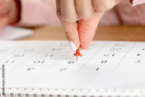 beautiful female Hand with manicure pushes a red pin on a calendar 9 day