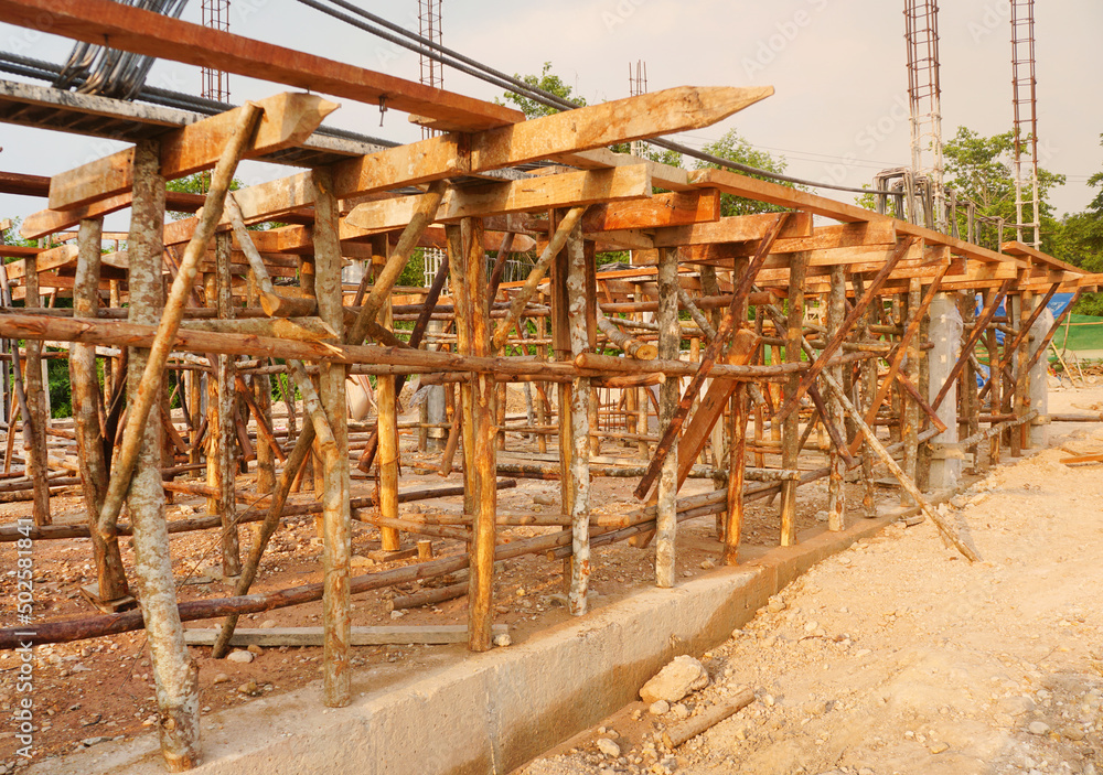 Temporary poles and wooden scaffolding support concrete beams at the house construction site.