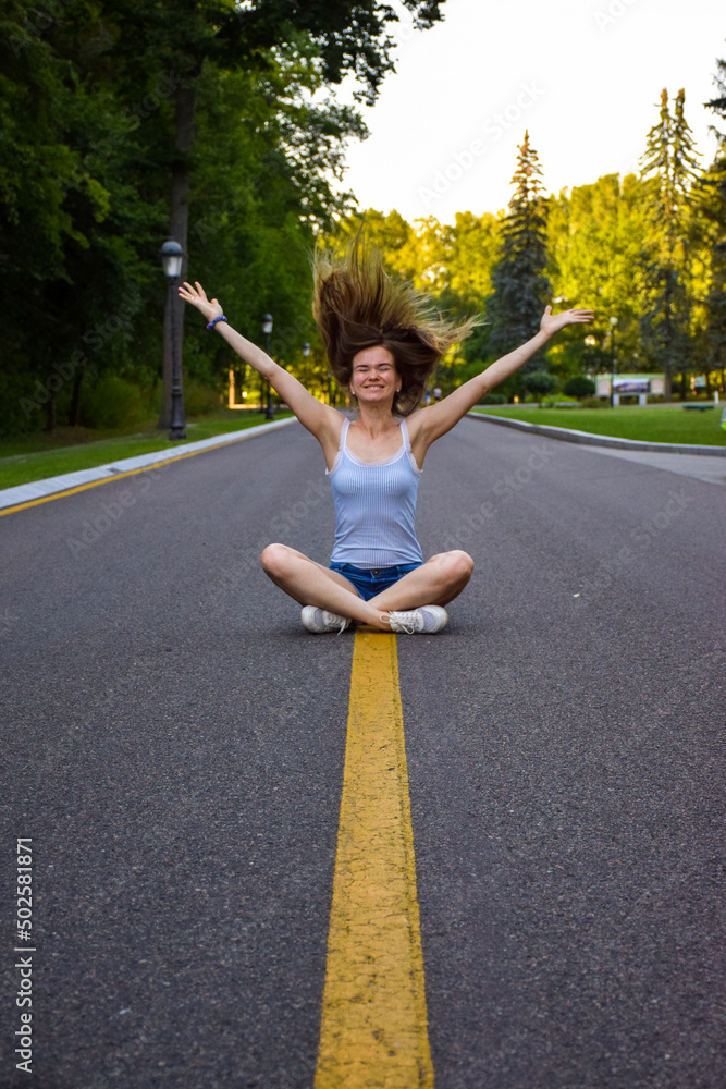 Funny emotional crazy girl goes crazy sitting on road in park with hands up and hair flying. Teenager scream from happiness and celebrate victory.