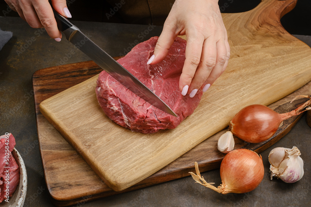 Chef cutting fresh raw meat on wooden board.  Shallow depth of field