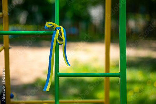 Ukrainian patriotic ribbon and a bouquet of dandelions on the playground, yellow and blue ribbon with flowers in memory of the dead children in Ukraine,