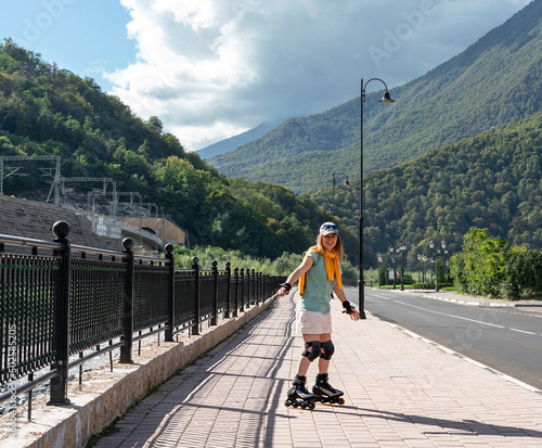 happy young woman in protective equipment riding on roller skates along embankment in summer active lifestyle, outdoor activities, roller skating