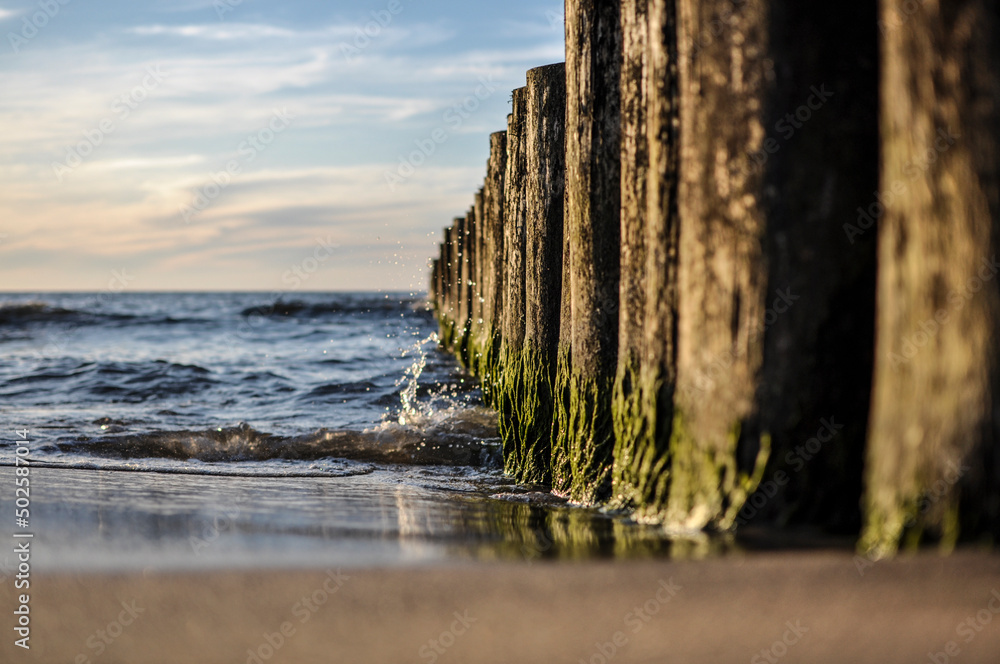 Sunset on the beach with breakwaters. - obrazy, fototapety, plakaty 