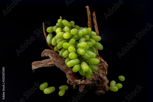 Green grapes isolated in black background lying on a wooden log with water drops shot in studio lighting photo