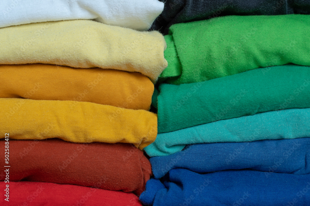 Stacks of multicolored fabrics in cool and warm colors are compared next to each other. Background with folded clothes with blank space for information. T-shirts of different colors Stacks of multicolored fabrics in cool and warm colors are compared next to each other. Background with folded clothes with blank space for information. T-shirts of different colors