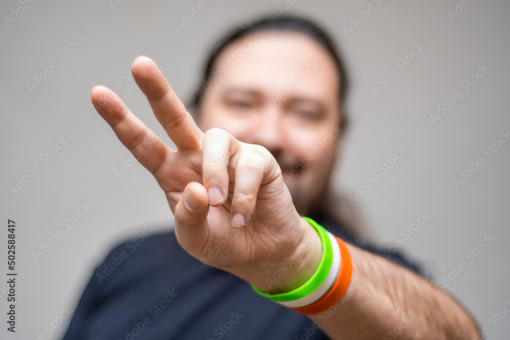 A smiling, unshaven man with bracelets in the colors of the Irish flag shows the victory sign. Selective focus on the bracelet. A smiling, unshaven man with bracelets in the colors of the Irish flag shows the victory sign. Selective focus on the bracelet.