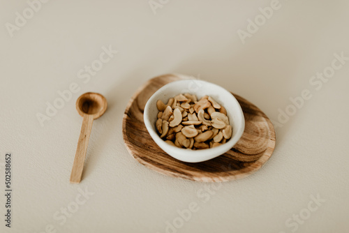 A ceramic bowl with roasted cashew nuts on a brown wooden plate on beige background with spoon. Top view. Healthy snack alternative, full with fiber, protein and vitamins. Copy space image.