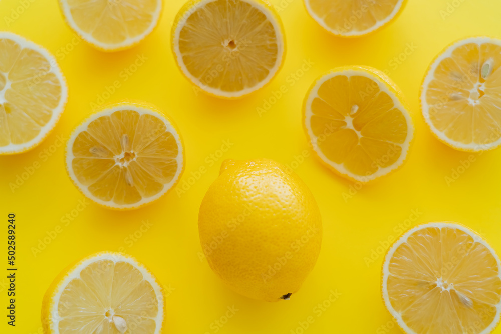 Top view of whole and halves of organic lemons on yellow surface